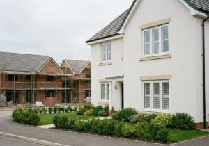 Completed new build home with plantation shutters, with houses under construction in the background — Cambridgeshire